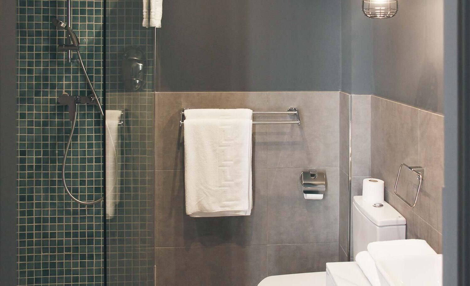 Un baño moderno con cabina de ducha de vidrio, inodoro con dispensador de toallas de papel y un perchero para toallas.