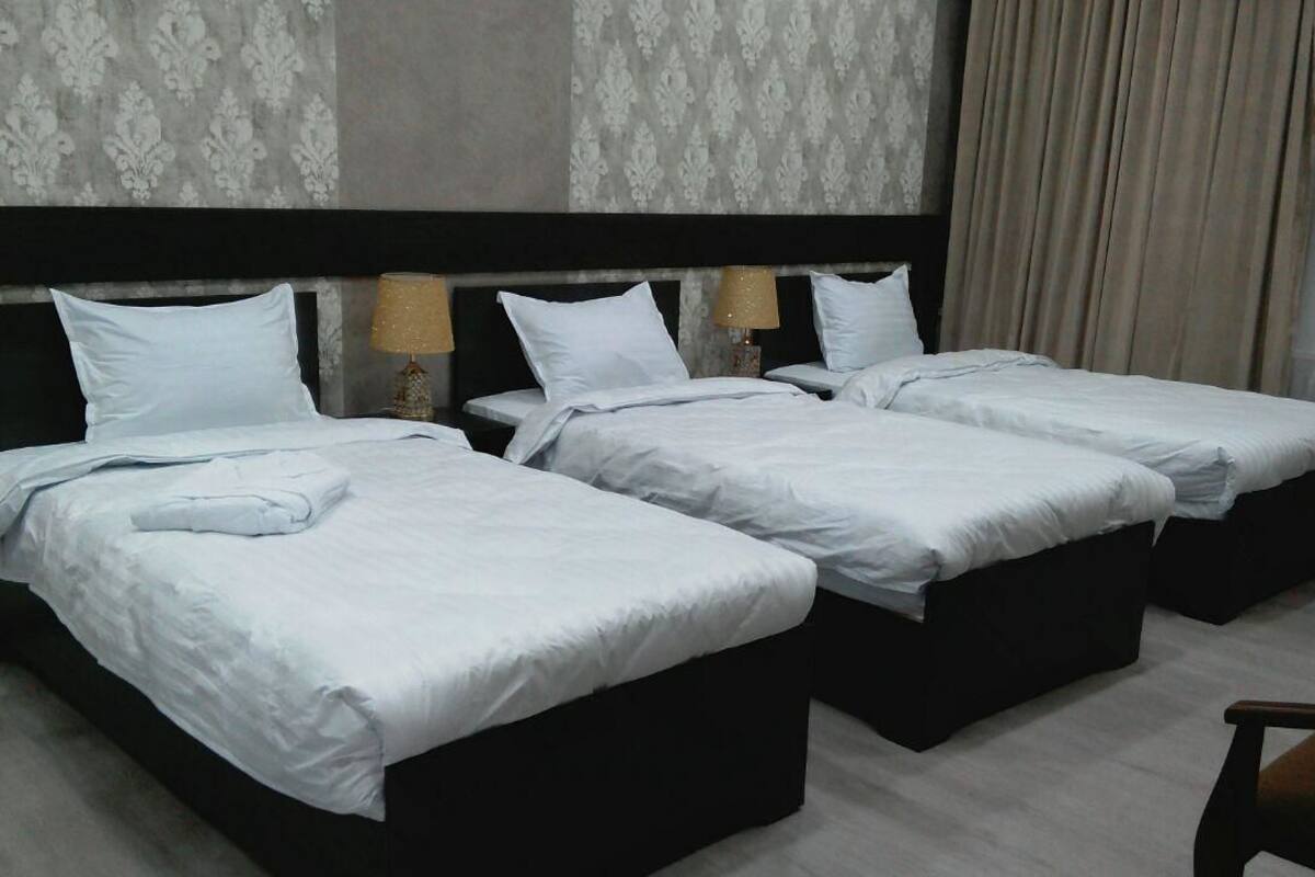A hotel room with three single beds, a dark headboard, and a chair.