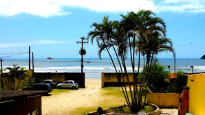 A patio with stone flooring and white chairs, overlooking a beach with palm trees and a view of the ocean. - Pousada Cantinho do Mar  (Guarujá)