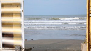 A beach view with a white building and a wooden fence. - Pousada Cantinho do Mar  (Guarujá)