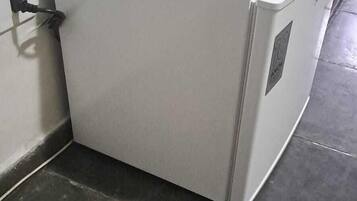 A white refrigerator in a corner of a room with dark tiled flooring.