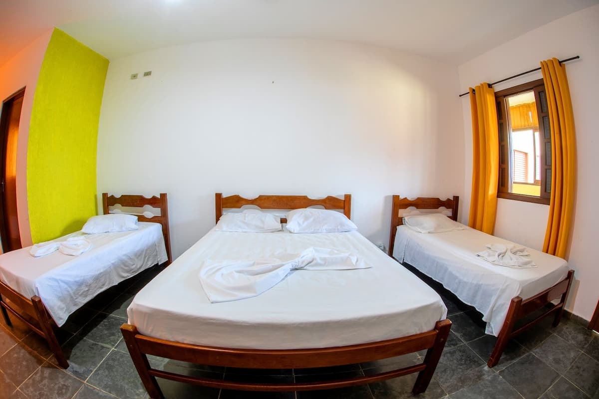 Una habitación con tres camas de madera, cada una con sábanas y almohadas blancas, dispuestas en fila.