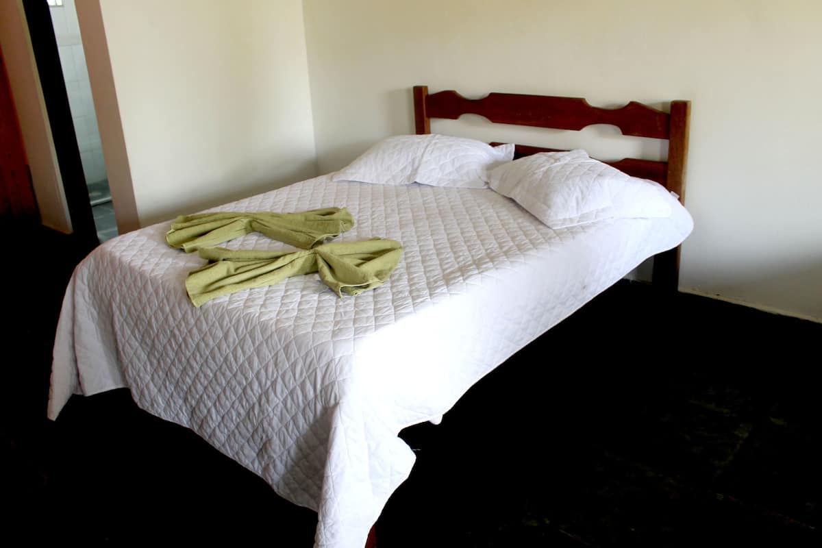 Una cama bien hecha con una colcha blanca acolchada y dos almohadas, un cabecero de madera y una toalla verde sobre la cama.