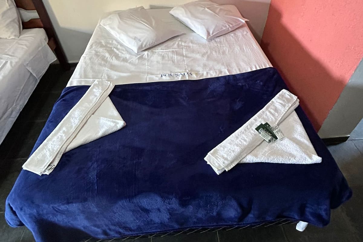 Una cama individual con una colcha azul y almohadas blancas, una manta blanca y una toalla doblada.