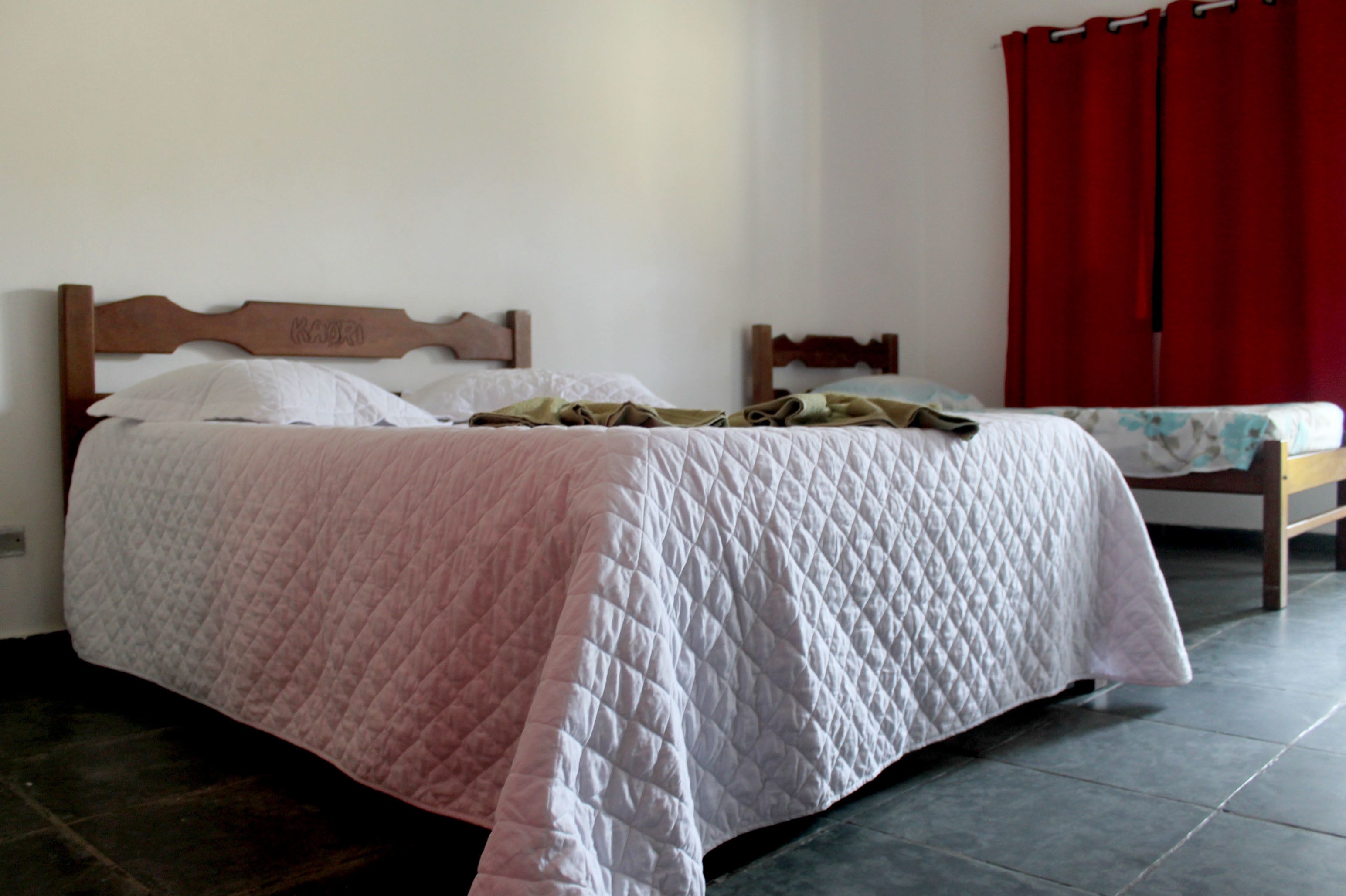 A single bed with a quilted bedspread, a wooden headboard, and a red curtain in the background.