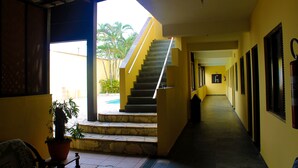A hallway with a staircase leading to a pool area, a potted plant, and a fire extinguisher on the wall. - Pousada Cantinho do Mar  (Guarujá)