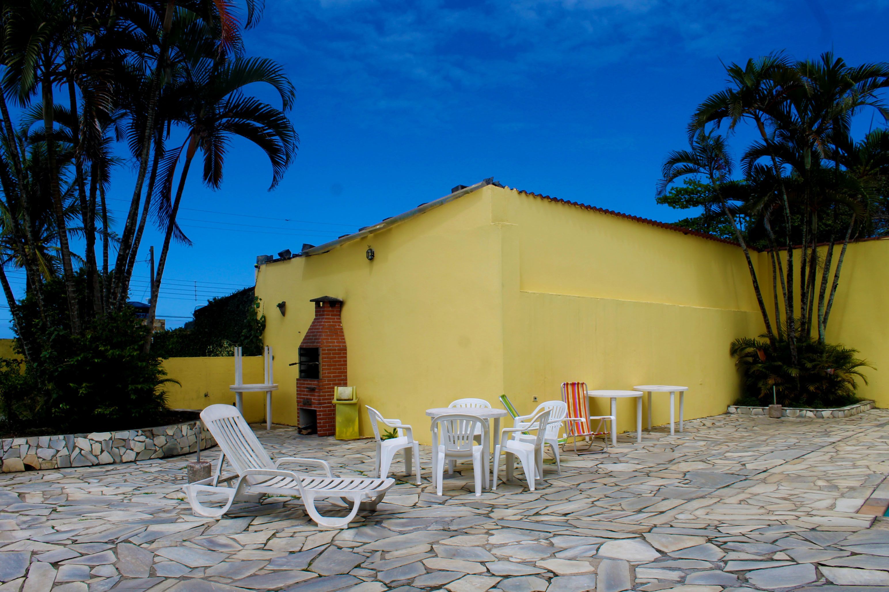 Um edifício amarelo com um alpendre de pedra, cadeiras e mesas brancas.