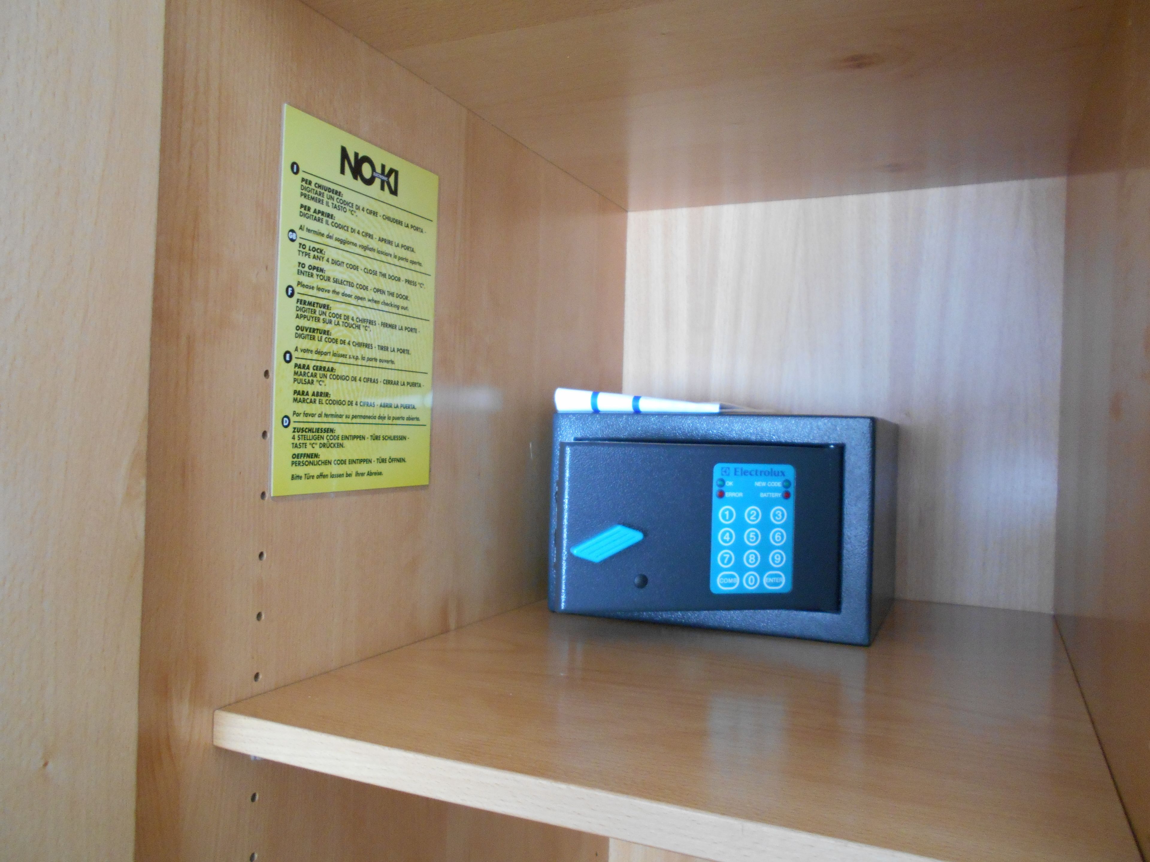 A wooden cabinet with a small electronic device on top, a yellow sign with instructions, and a white shelf below.
