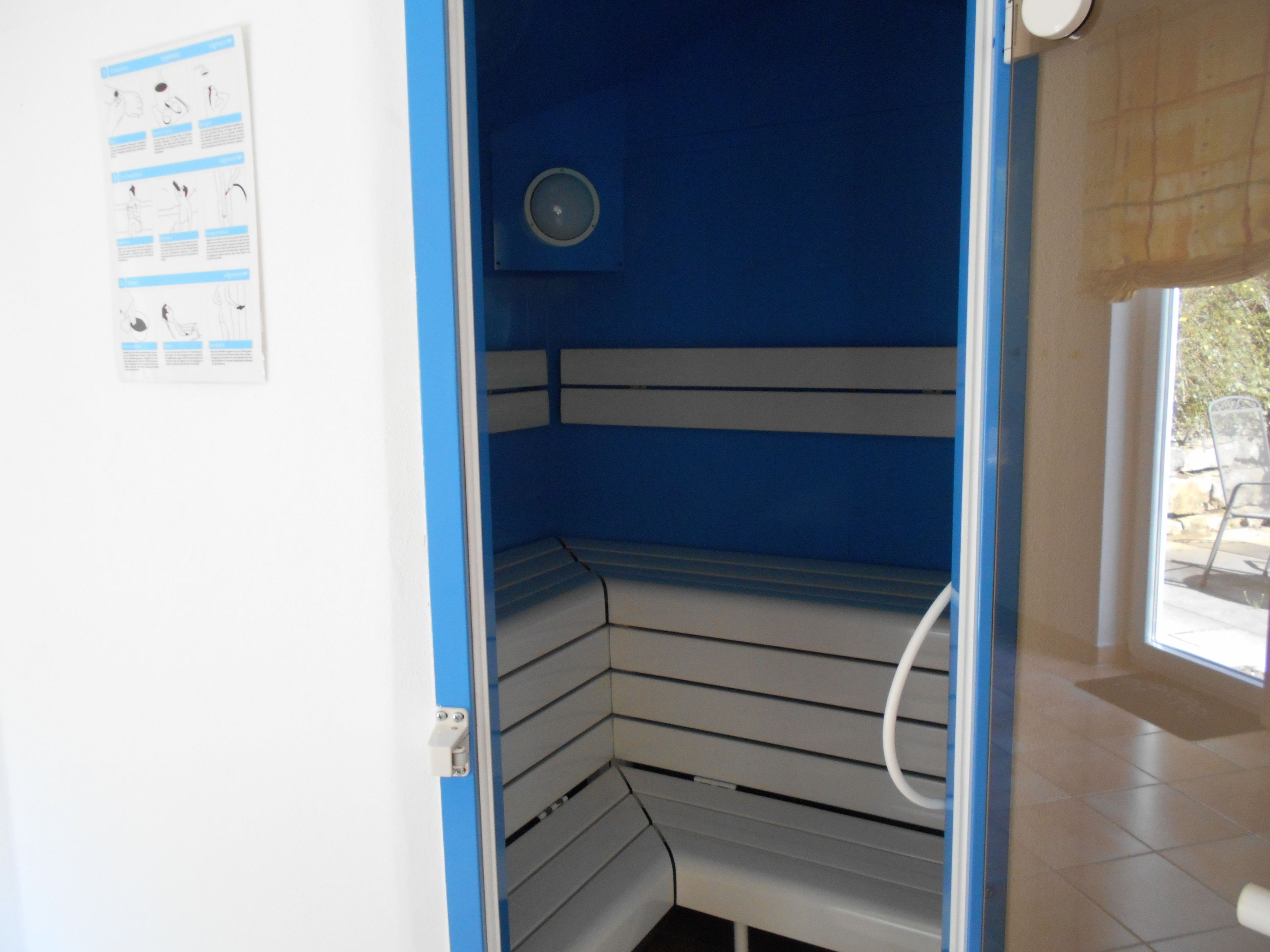 A sauna room with a blue interior, a ceiling fan, and a window with a view of the outside.
