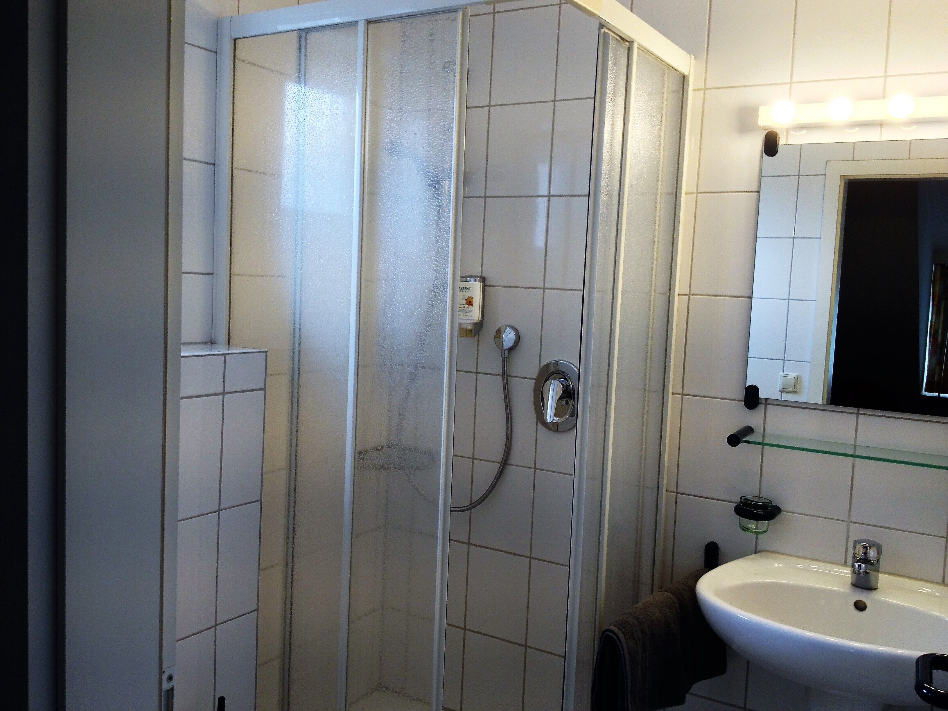 Un bagno con cabina doccia in vetro, lavandino bianco e specchio sopra il lavandino.