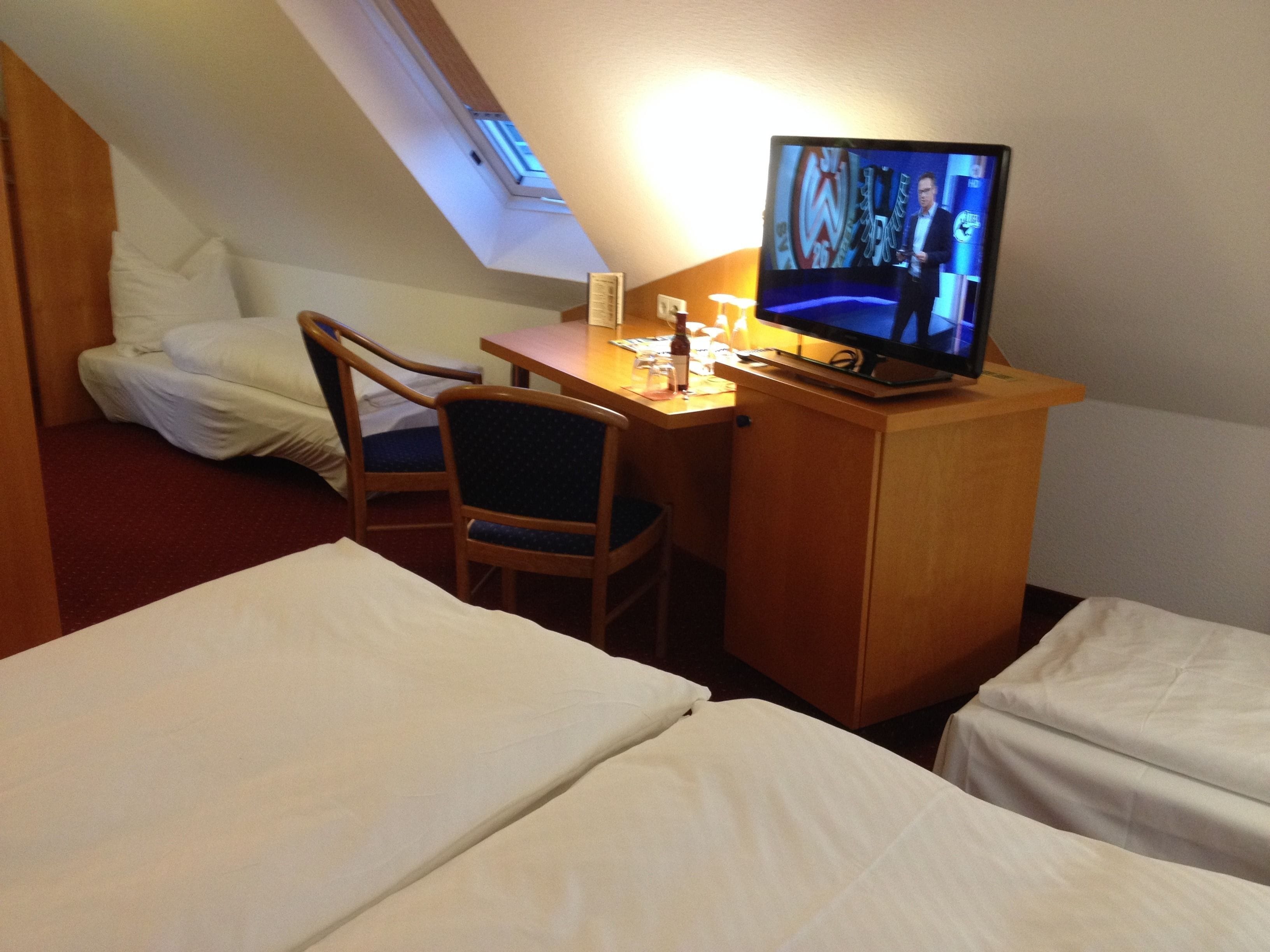 A hotel room with a desk, a television, two beds, and a chair.