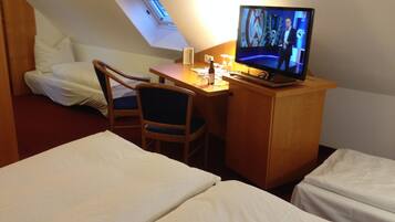 A hotel room with a desk, a television, two beds, and a chair.