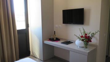 Ein Hotelzimmer mit Bett, Schreibtisch mit Flachbildfernseher, Blumen in einer Vase und einem Fenster mit Vorhängen.