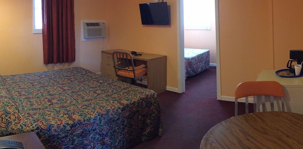 A hotel room with a bed, a desk, a chair, a small table with a cup, and a television on the wall.