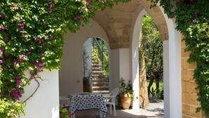Un patio al aire libre con mesa y sillas, arcos de piedra y plantas en macetas.