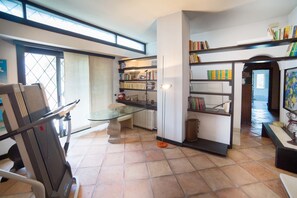A spacious room with a glass table, a treadmill, and a bookshelf filled with books.