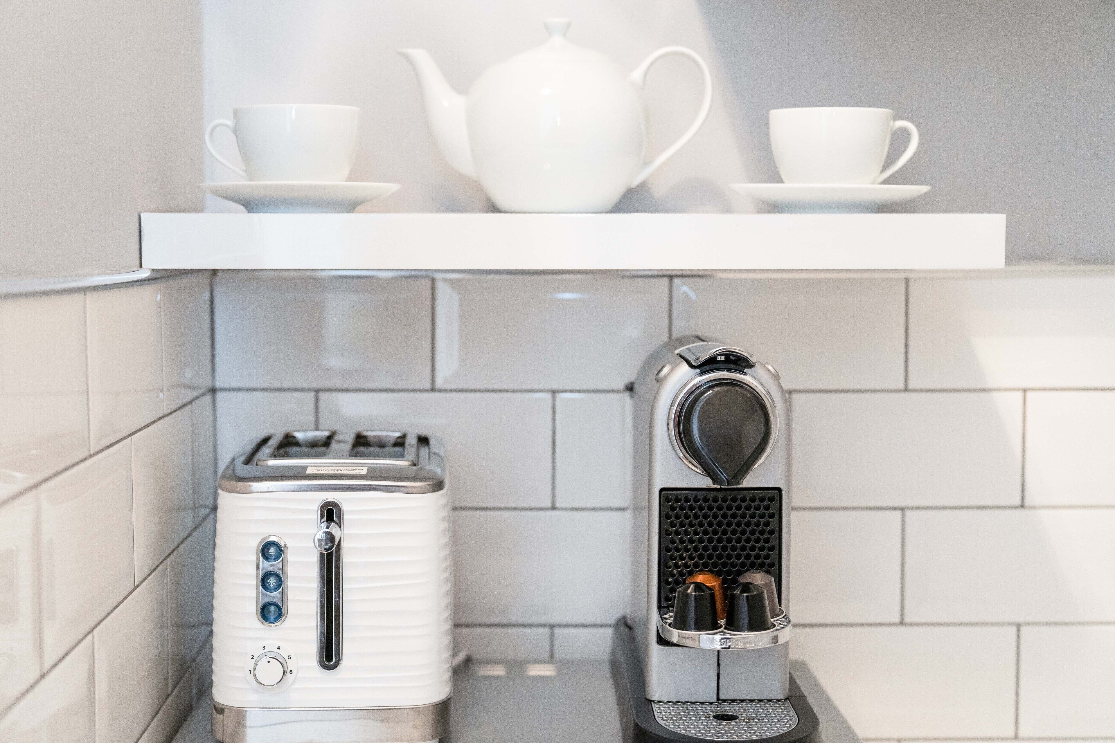 A kitchen with a white toaster, a coffee maker, and a white teapot on a shelf.