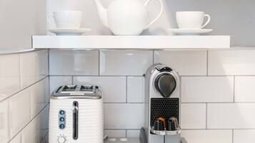A kitchen with a white toaster, a coffee maker, and a white teapot on a shelf.