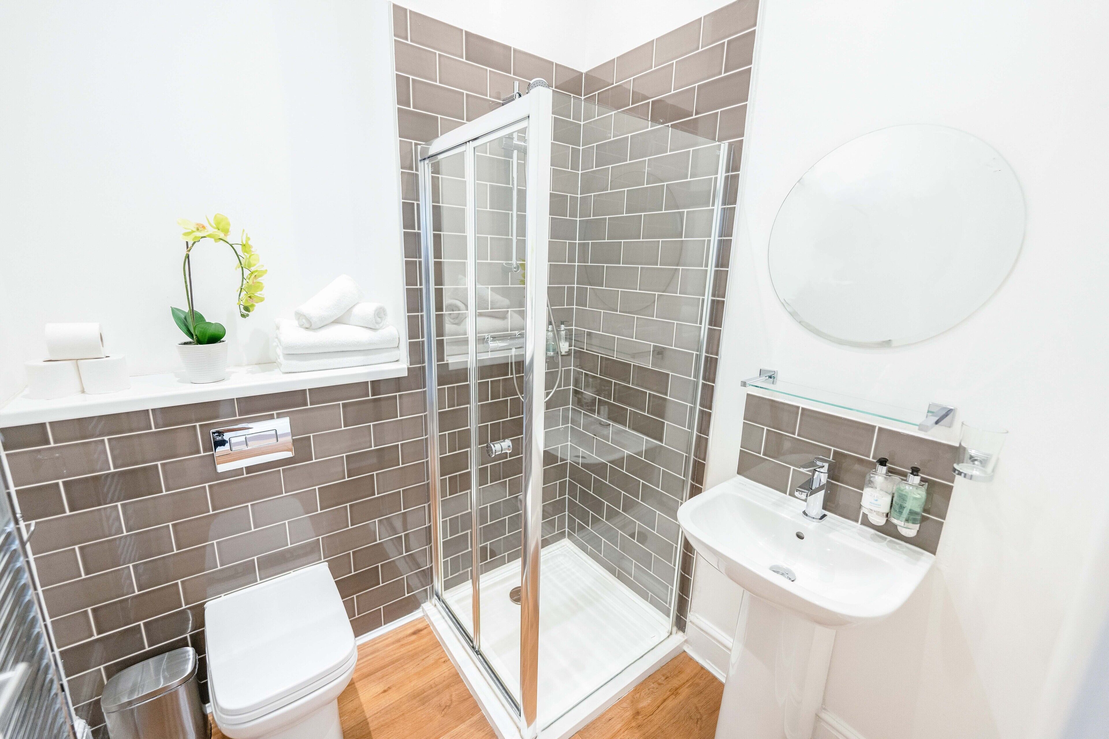 Un baño moderno con ducha de vidrio, lavabo blanco y una pequeña planta en maceta.