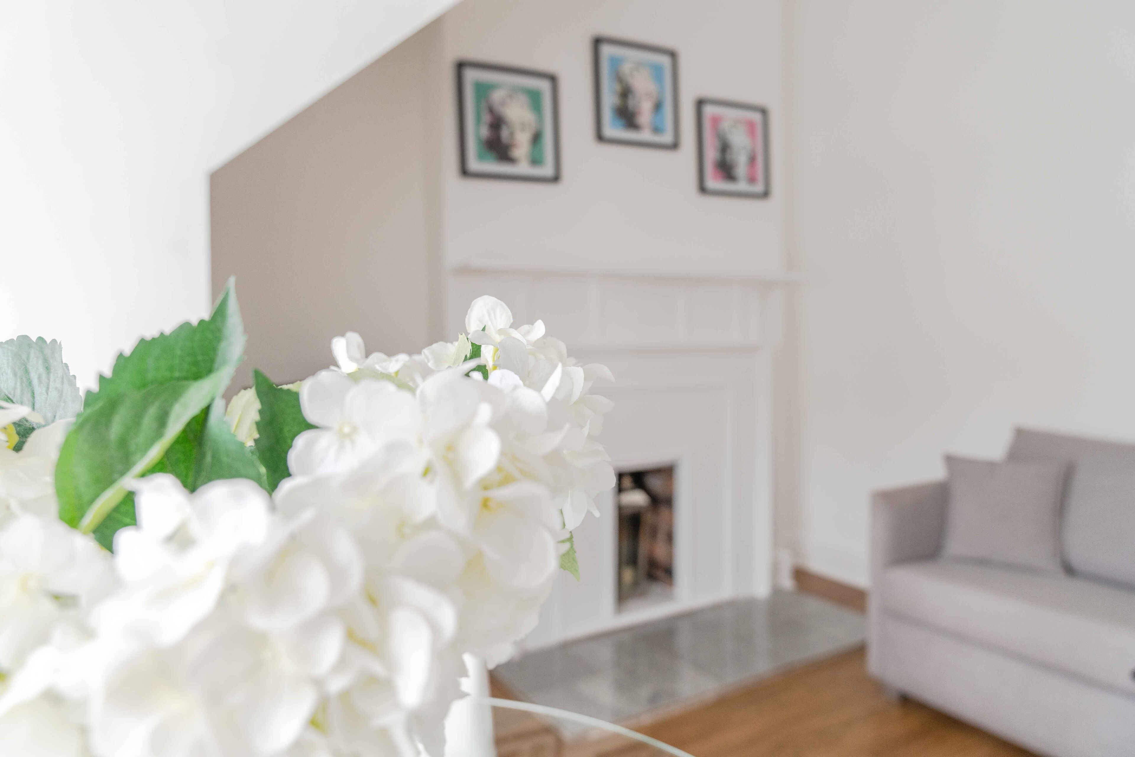 Een woonkamer met een witte bank, een open haard en ingelijste foto's aan de muur.