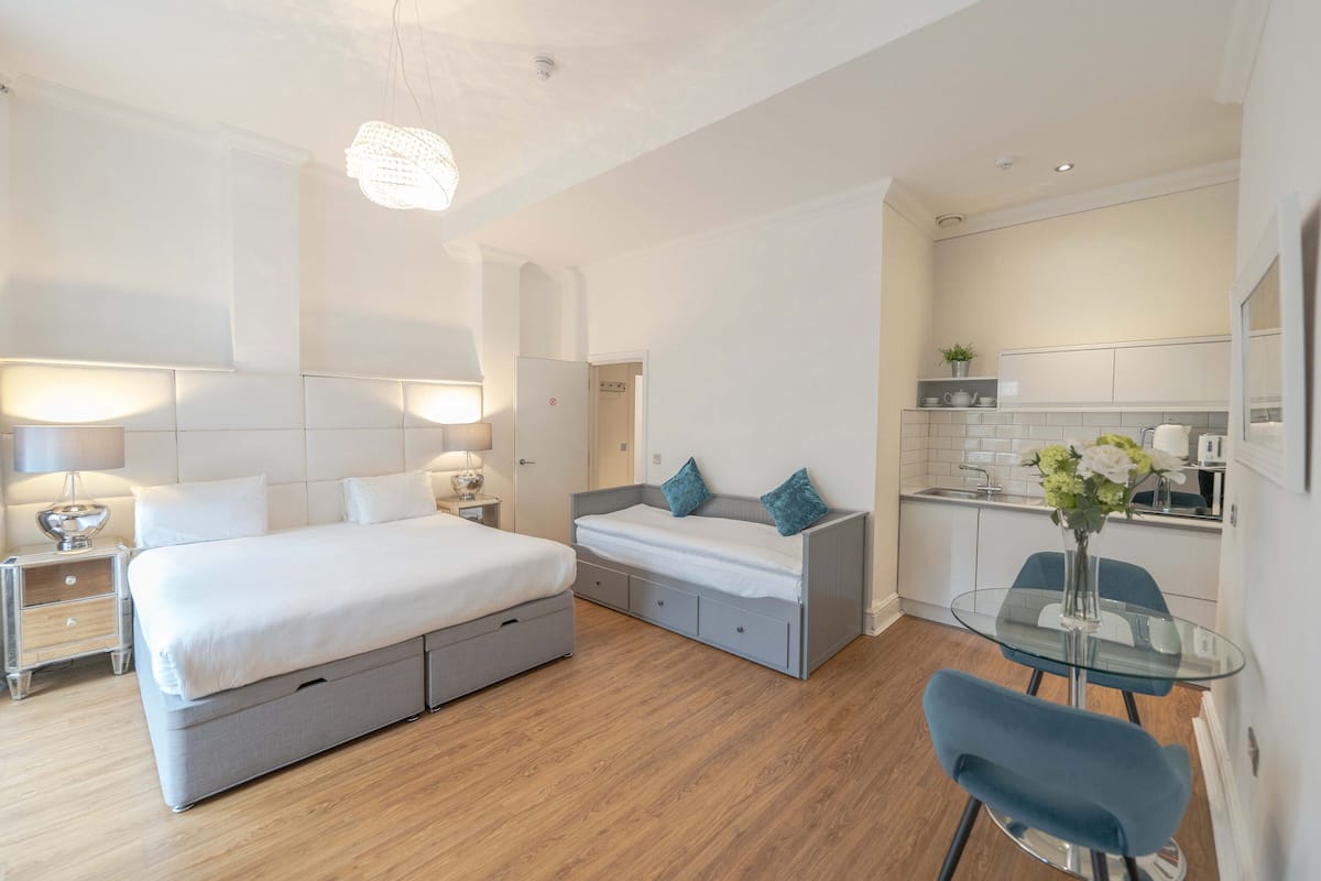 A modern bedroom with a large bed, bedside tables, a small sofa, and a glass dining table.