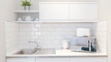 Una cocina moderna con muebles blancos, un lavamanos de acero inoxidable, una tetera y un microondas.