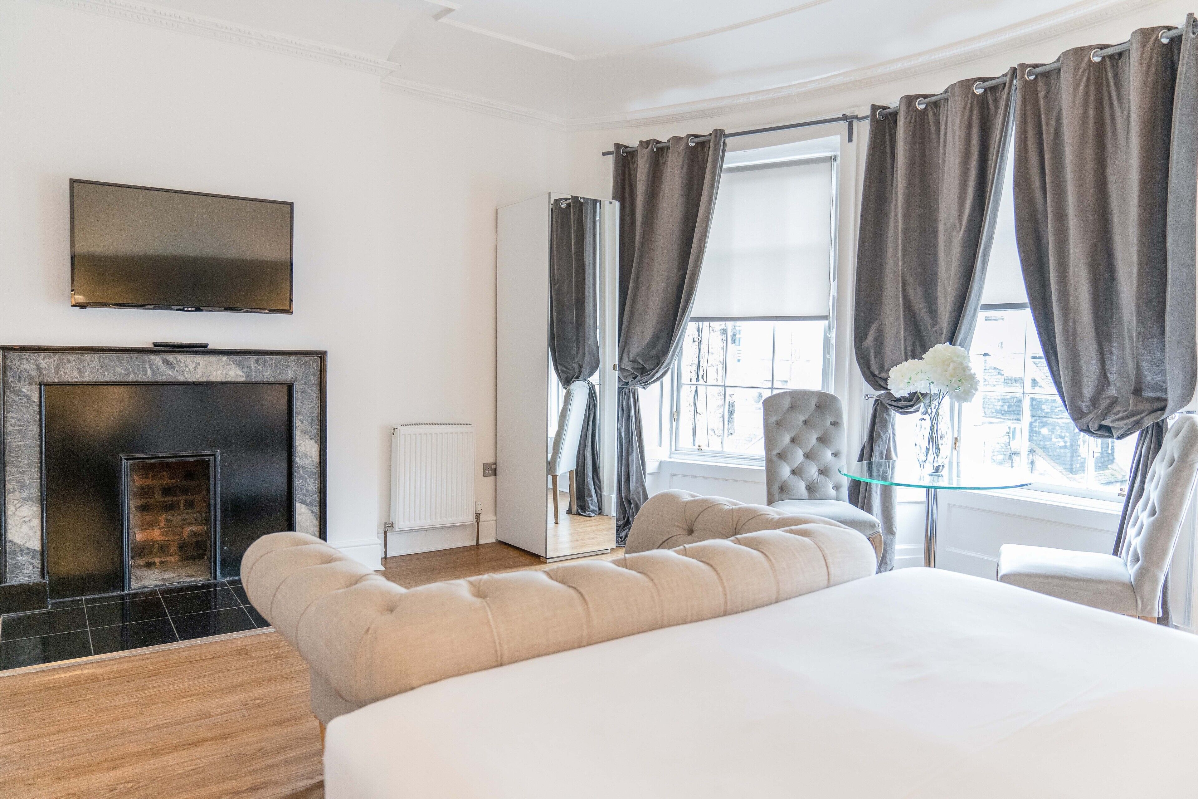 Une chambre d’hôtel moderne dotée d’un grand lit, d’une télévision à écran plat, d’une cheminée et offrant une vue sur la ville grâce à de grandes fenêtres.