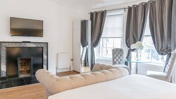 Une chambre d’hôtel moderne dotée d’un grand lit, d’une télévision à écran plat, d’une cheminée et offrant une vue sur la ville grâce à de grandes fenêtres.