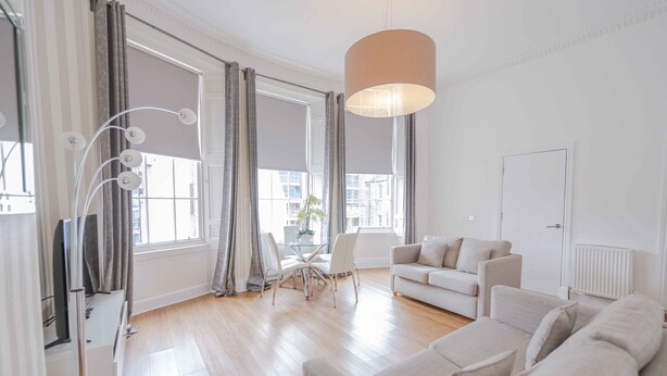 Una sala moderna con un sofá, una mesa de comedor con sillas y un ventanal con cortinas.