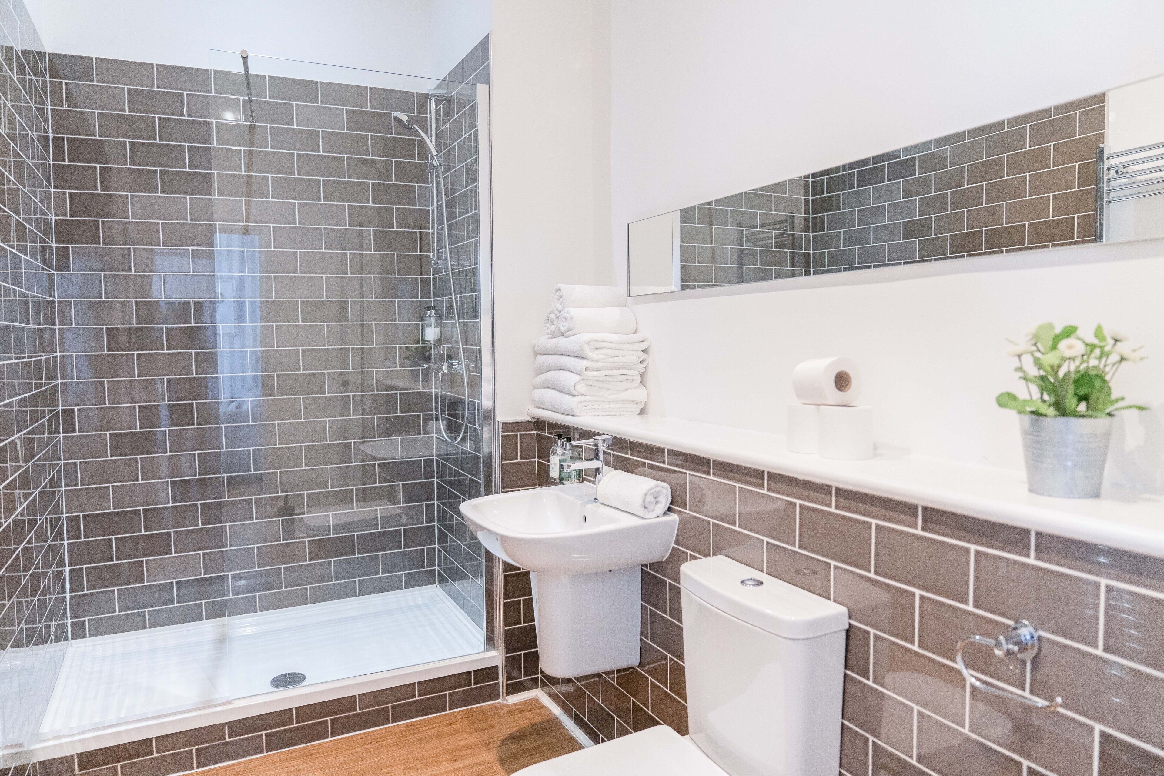 Een moderne badkamer met een douchecabine van glas, een witte wastafel en een toilet.