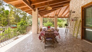 An outdoor patio with a stone floor, wooden ceiling beams, and a table set for dining. - Villa Pizzi (San Donaci)