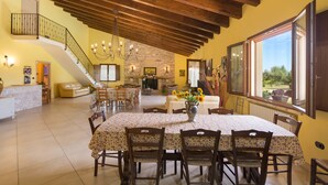 A spacious dining area with a high ceiling and exposed beams, a fireplace, and a view of the outdoors through a large window. - Villa Pizzi (San Donaci)