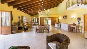A spacious living area with a high wooden ceiling, a chandelier, and a dining area with a table and chairs. - Villa Pizzi (San Donaci)