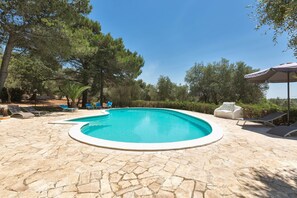A swimming pool with stone tiles, surrounded by lounge chairs and a shaded area.
