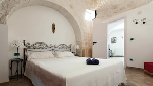 A bedroom with a large bed, a stone arch, a white wall, and a door leading to another room. - Villa Ricci (Ceglie Messapica)