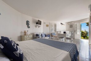 Un dormitorio con cama, mesita de noche, cómoda, escritorio, silla y vistas a través de una puerta abierta.