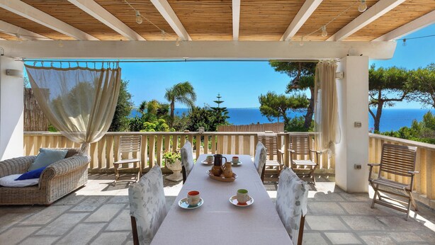 Terraço com mesa posta para refeições, vista para o mar.