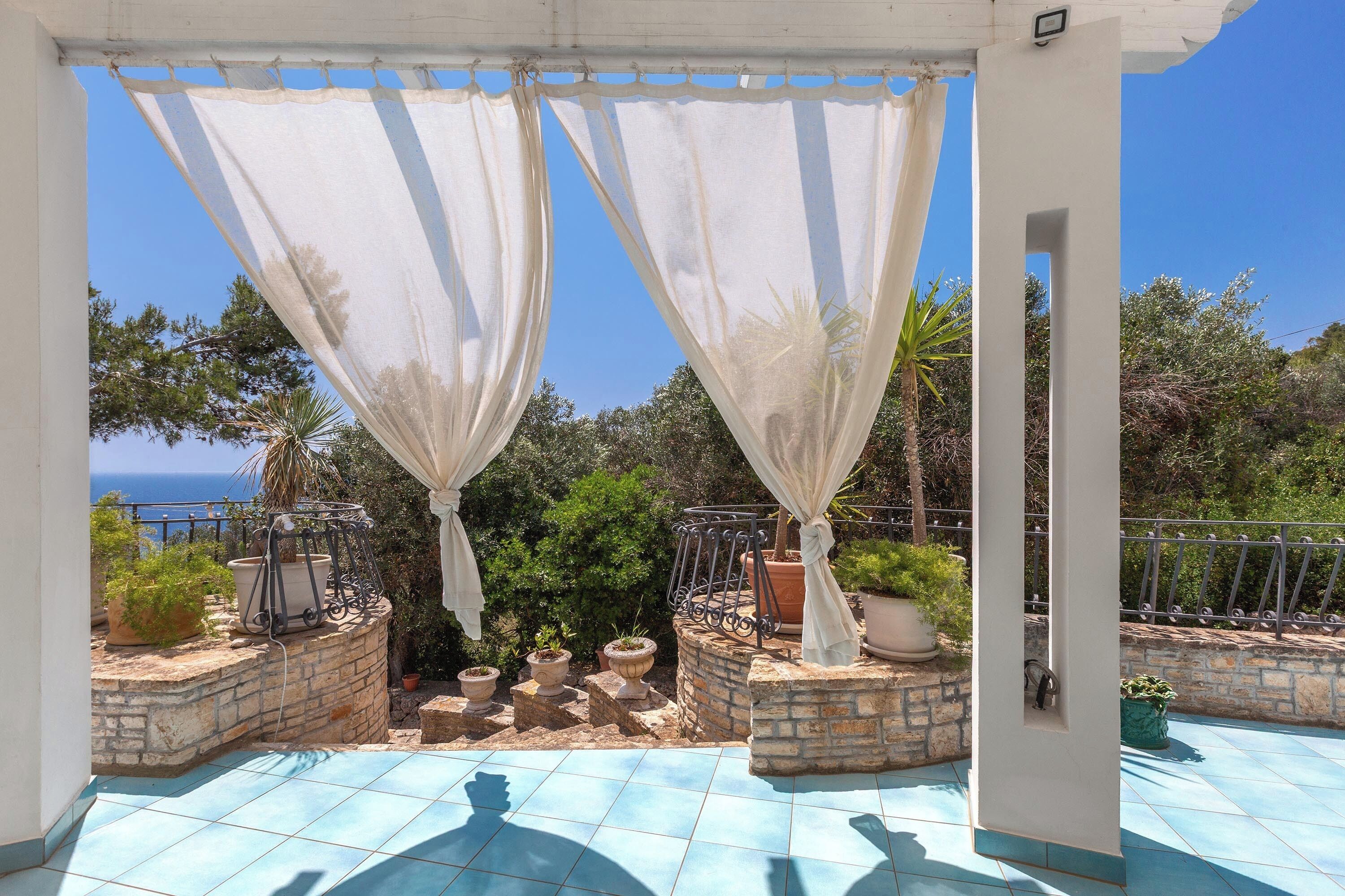A covered outdoor area with potted plants and a view of the sea.
