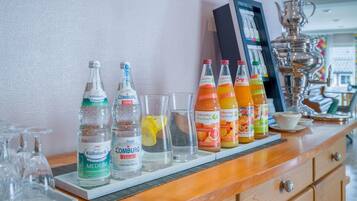 Un espace bar avec différentes bouteilles d’eau et de jus, des verres et un pichet décoratif en argent.