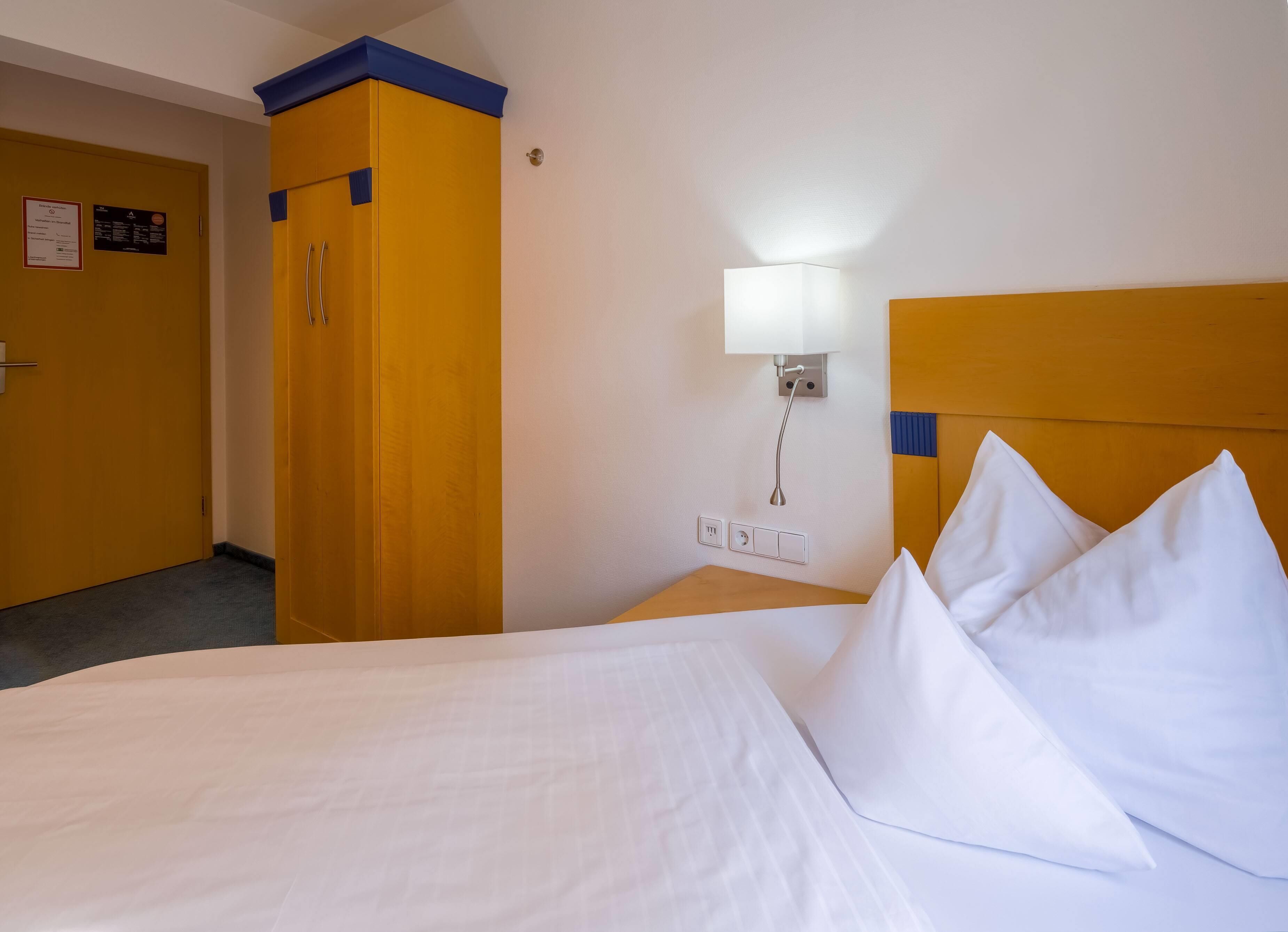 Una habitación de hotel con una cama, una mesita de noche, una lámpara y un armario.