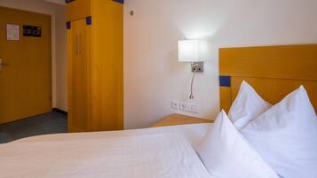 Una habitación de hotel con una cama, una mesita de noche, una lámpara y un armario.