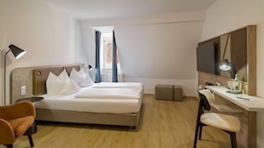 A modern hotel room with a large bed, a desk, a chair, a lamp, and a television. - Aspire Kronprinz, Trademark Collection by Wyndham (Schwäbisch Hall)