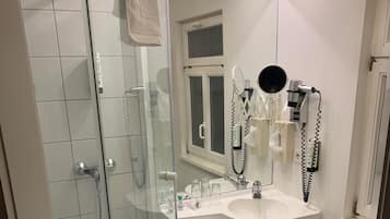 Een badkamer met een douche met glazen wand, een wastafel met spiegel en een aan de muur bevestigde haardroger.