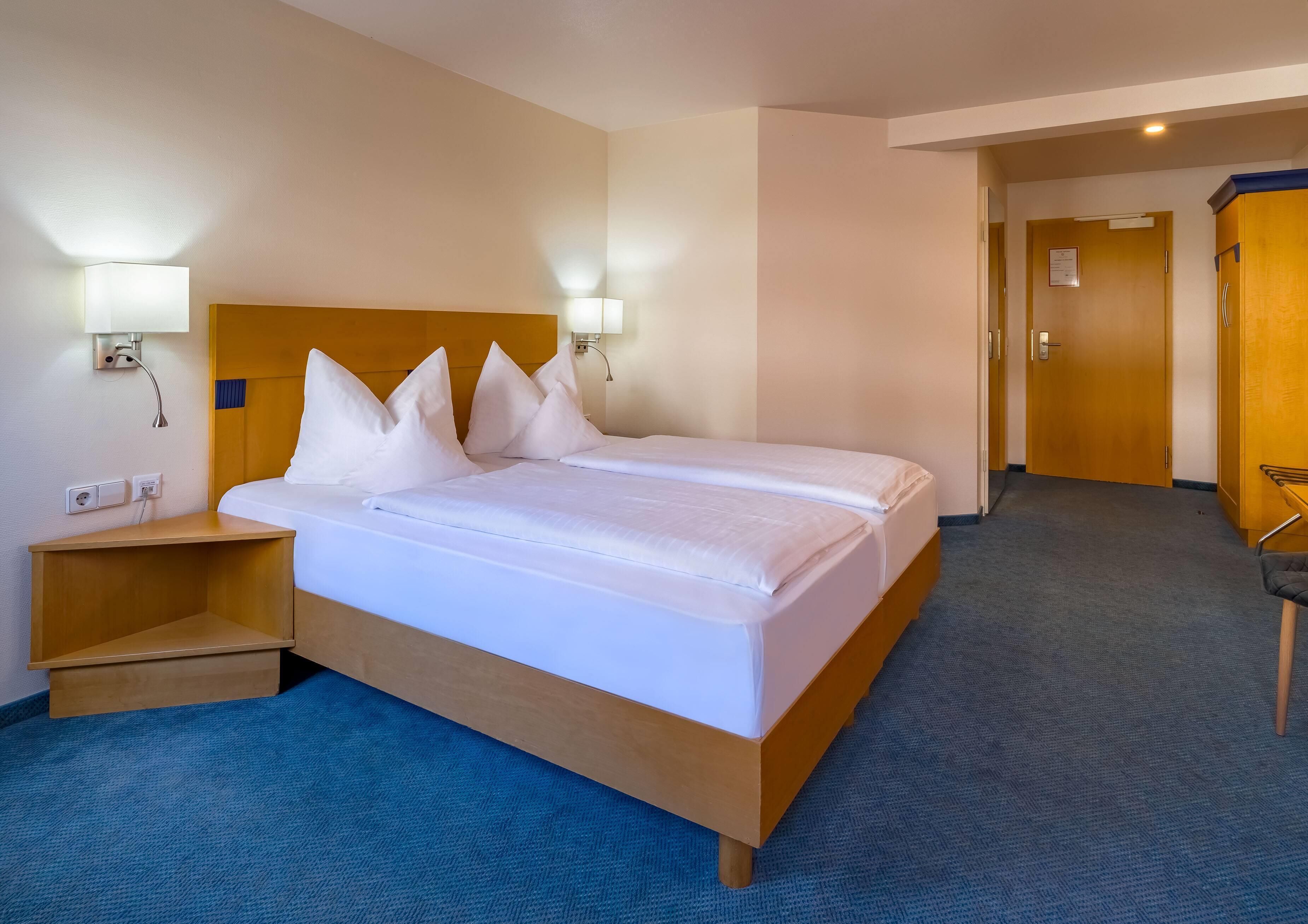 A hotel room with a large bed, bedside tables, and a carpeted floor.
