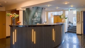 A reception desk with a modern design, a large sign reading "Aspire Hotel," and a vase with flowers. - Aspire Kronprinz, Trademark Collection by Wyndham (Schwäbisch Hall)