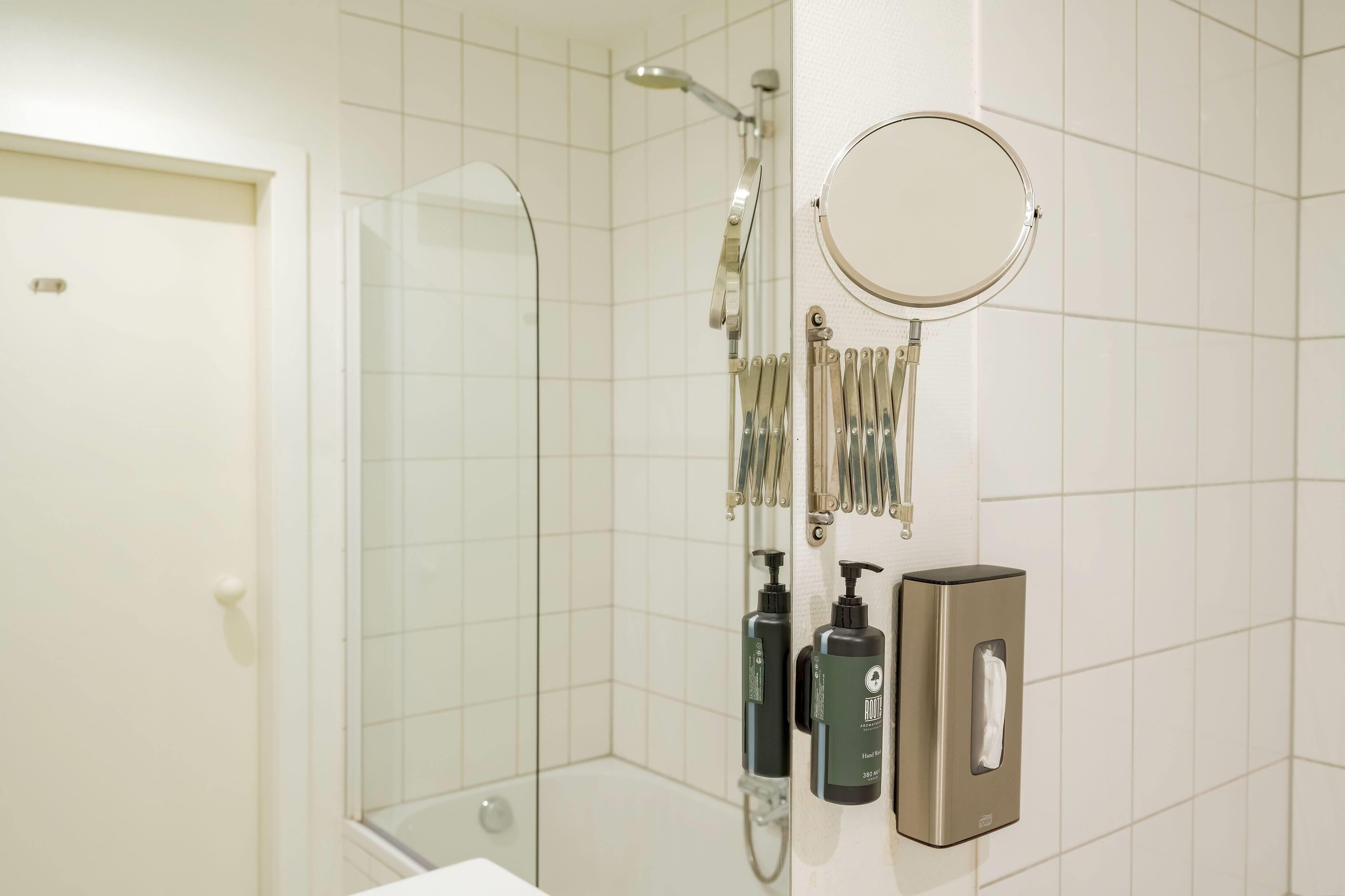 A bathroom with a glass shower enclosure, a handheld showerhead, a wall-mounted mirror, and toiletries including shampoo and soap dispensers.
