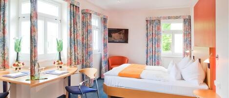 A hotel room with a bed, desk, chair, and a window with curtains.