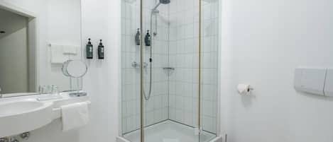 Un baño moderno con cabina de ducha de vidrio, un lavabo blanco y un inodoro.