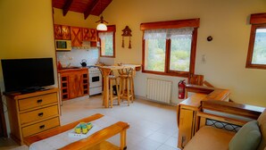 Uma sala de estar aconchegante com um banco de madeira, uma TV e um espaço de refeições com mesa e cadeiras.