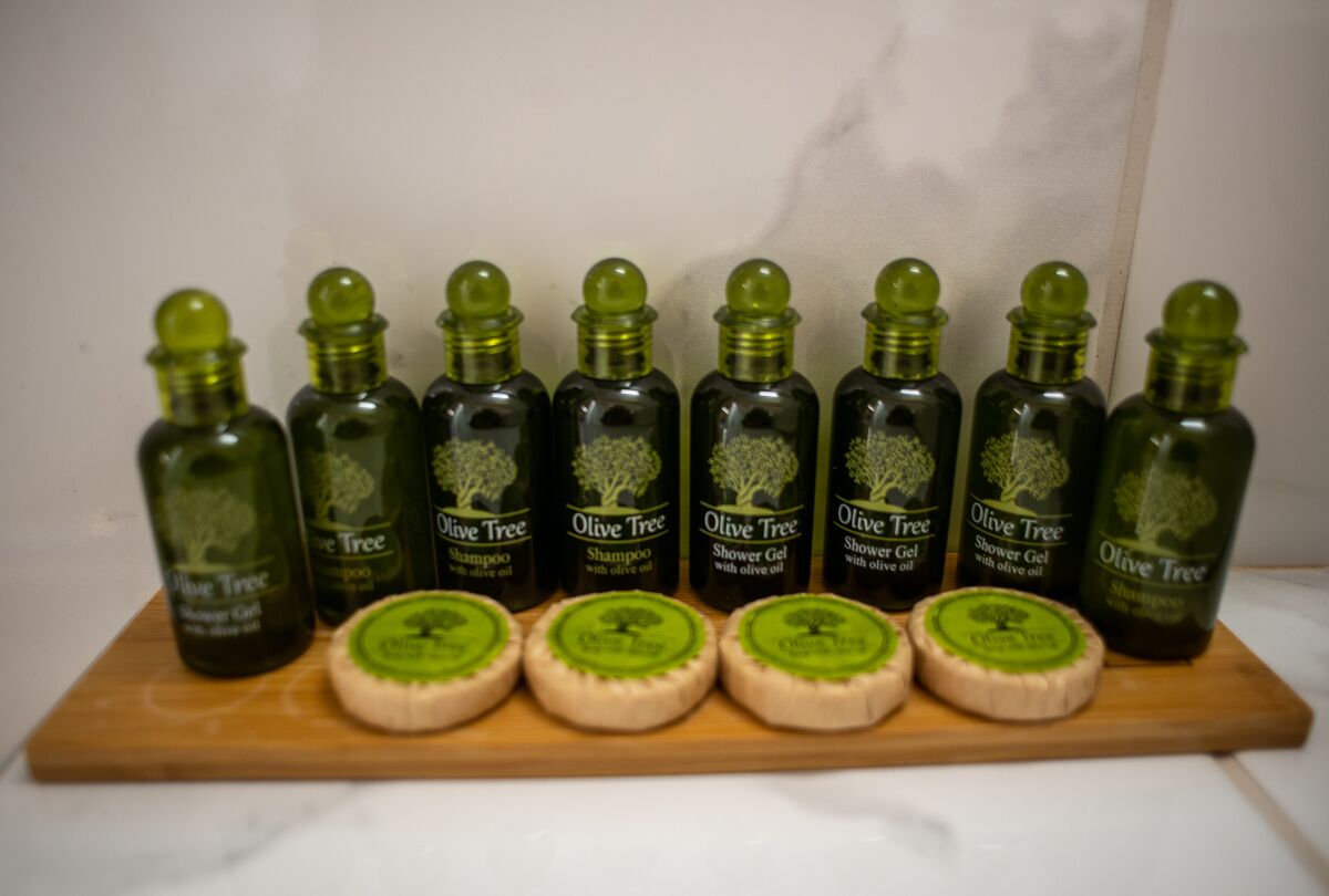 A wooden board with eight bottles of Olive Tree products and four soaps.